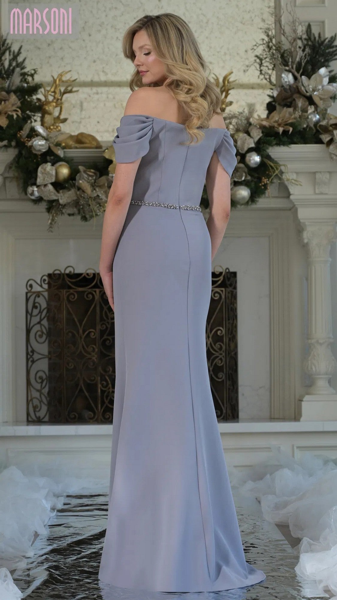 A woman wearing the Marsoni MV1352, a long formal dress featuring an off-shoulder neckline and a beaded waistband.